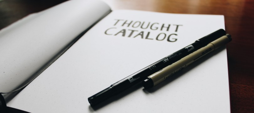 An open book with unlined paper and the words "thought catalogue" written in block letters at the top. Two black markers are resting on the page.
