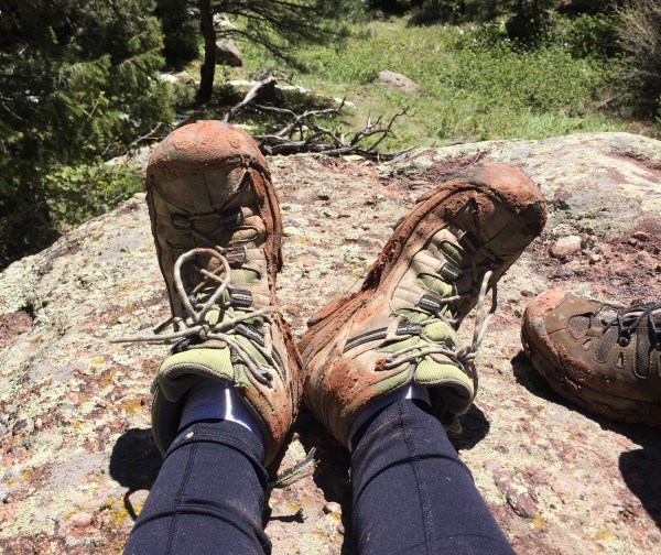 muddy-hiking-boots-on-feet-of-hiker-sitting-on-large-rock
