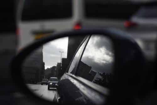 car side mirror with city and other cars in reflection