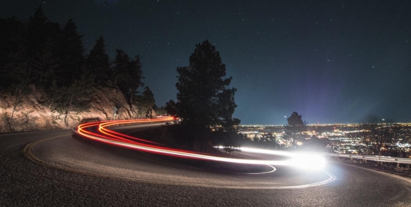 nighttime time lapse of mountain road curving and car lights driving around pine tree