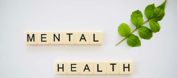 scrabble tiles reading Mental Health with sprig of greenery on side