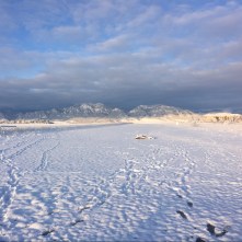 rocky mountains under blue sky with clouds and snowy plains in front