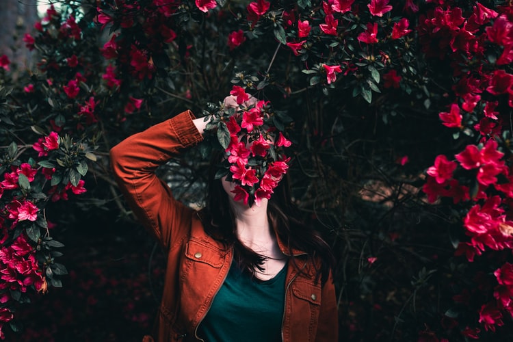 woman in orange jacket holding flowers in front of face