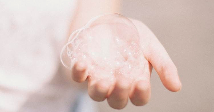 extended-hand-holding-soap-bubbles-with-beige-background