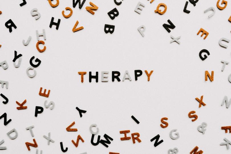 Black, grey, and orange alphabet letters scattered around the word therapy
