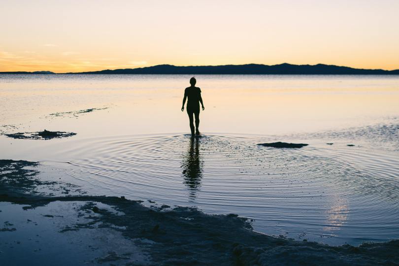 Silhouette of a person walking into a lake at sunset with ripples on the water and a view of the horizon