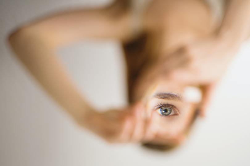 A blurry woman holding a magnifying lens up to her eye so that her body is upside down and her eye is right side up.