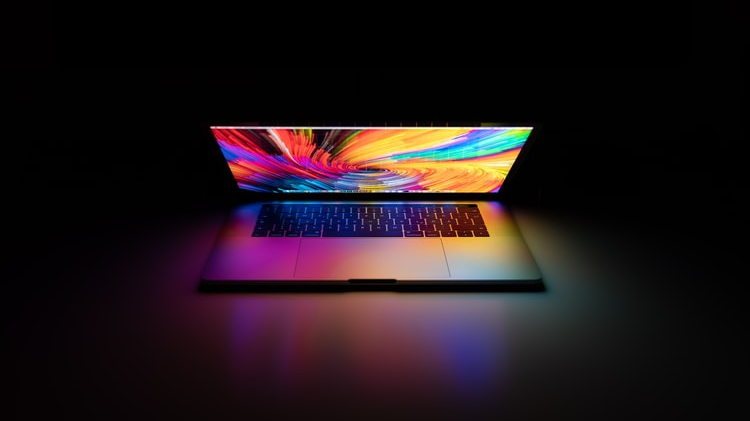An open laptop with the screen angled down and a bright swirl of colors being displayed against a dark background