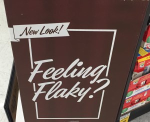 A brown cardboard sign with white letters in cursive that say "feeling flaky?"