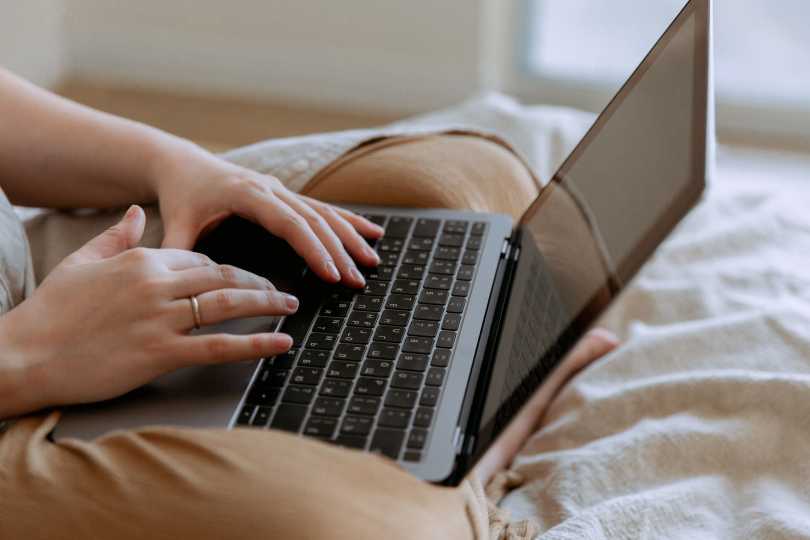A laptop on a woman's lap while she sits cross legged and uses the trackpad