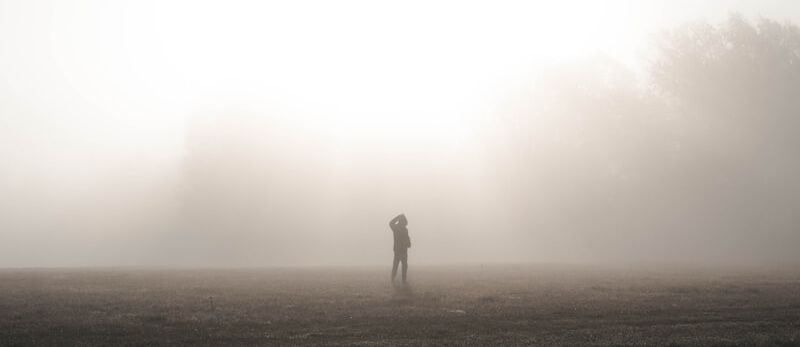 The silhouette of a person standing in a field in a thick fog.