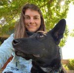 A young woman smiling while taking a selfie with a black dog with pointy ears.