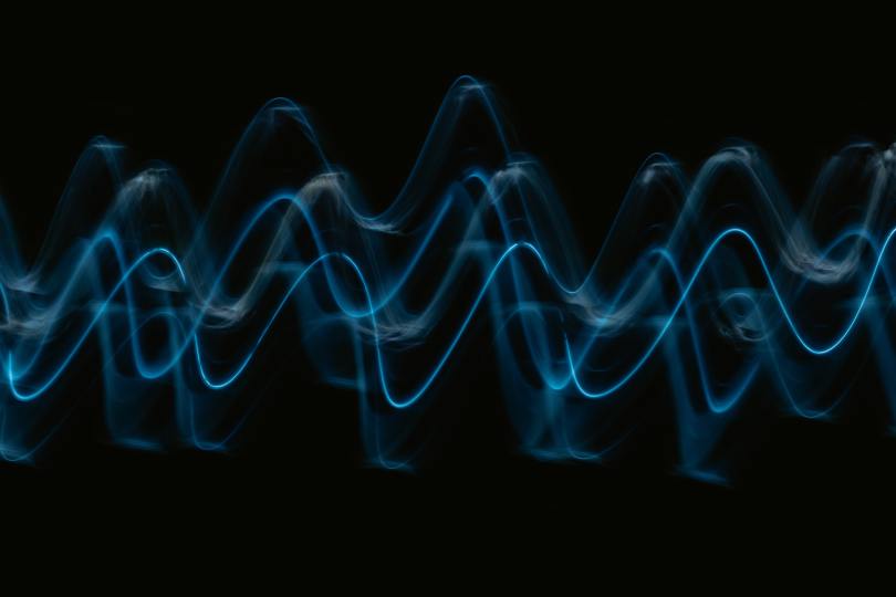 Long exposure blue lights in the shape of sound waves against darkness
