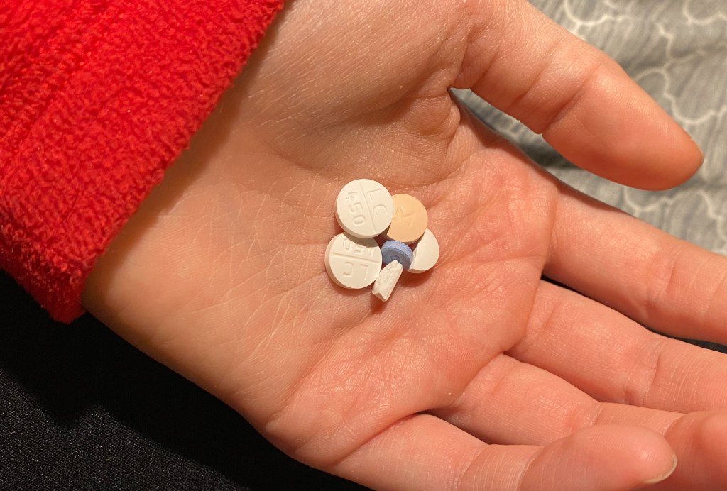 A hand holding several pills of different sizes and colors in its palm.